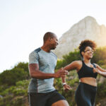 Sports, workout and couple walking by a mountain training for a race, marathon or competition. Fitness, nature and athletes doing an outdoor cardio exercise for health, energy and endurance at sunset.